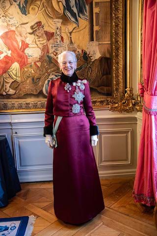Dronning Margrete av Danmark smiler iført lille lang kjole i et herskapelig rom