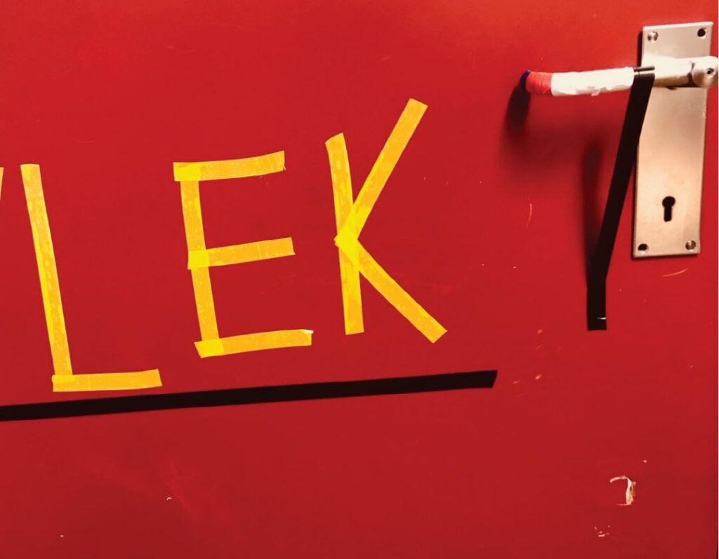 Bokstavene L E K tapet opp med gul tape på en rød dør
