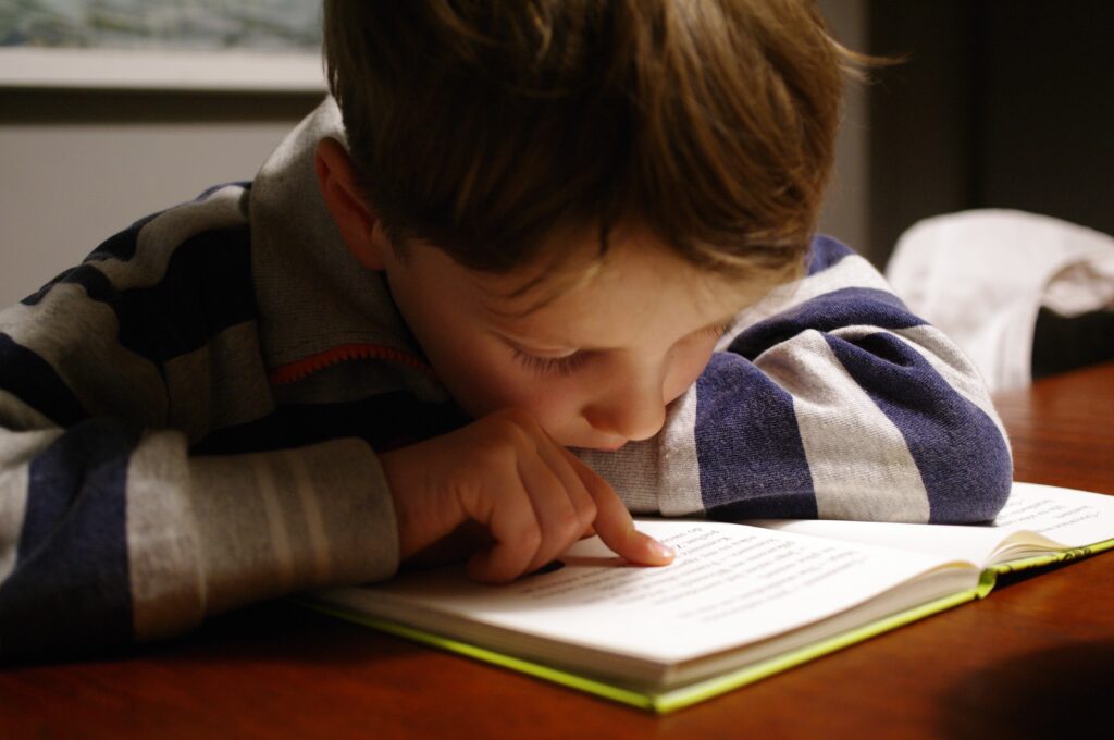 Liten gutt sitter bøyd over en bok og leser.